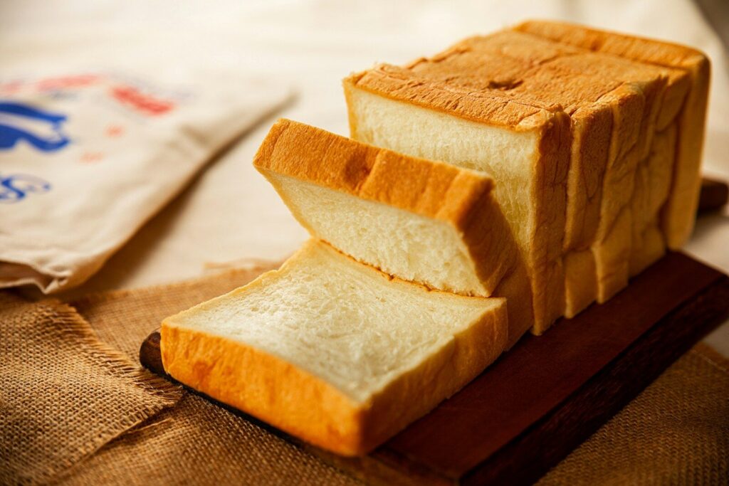 A loaf of sliced white bread on a wooden board with burlap